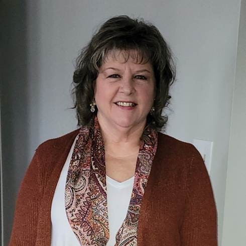 Woman in brown sweater and paisley scarf smiling indoors.