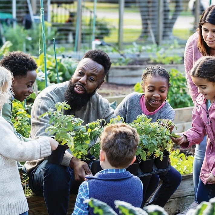 Group of children and adults planting seedlings in a community garden.